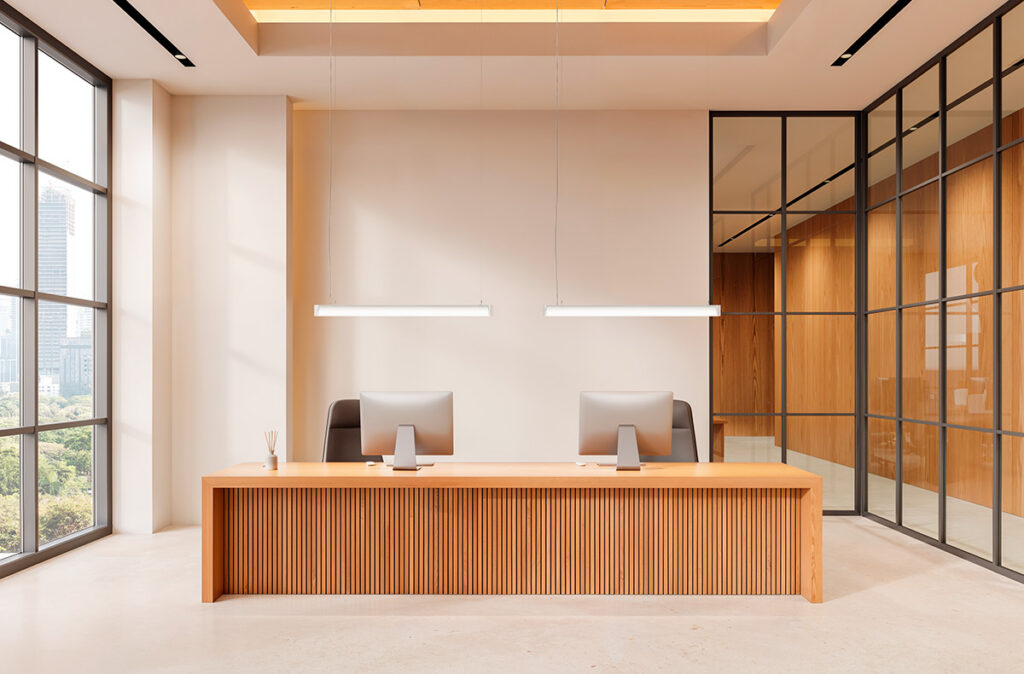 Två slanka linjära LED-pendellampor från PROLJUS AB hänger över en receptionsdisk och ger jämnt varmvit ljus som lyfter den moderna minimalistiska kontorsmiljön, energieffektiva och stilrena armaturer perfekta för kontor och entréer