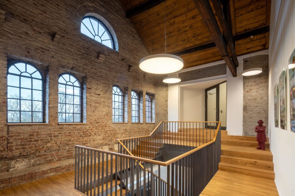 Tre runda, hängande LED-armaturer från PROLJUS AB ger varmt, jämnt nedåtriktat ljus i en renoverad industrilokal och framhäver trappan och träbjälkarna, idealiska för kontor och offentliga miljöer