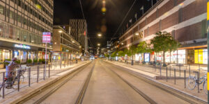 Centrala Stockholm nattetid med spårvagnsspår, Åhléns varuhus, upplysta butiker, cyklar och hållplatser.