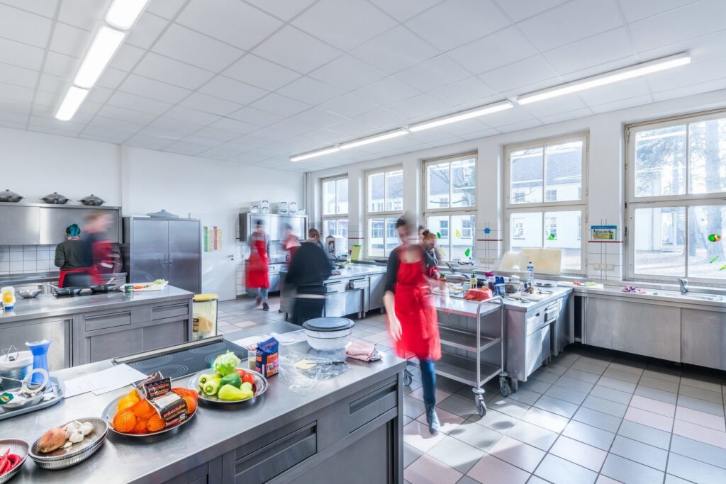 Väl upplyst undervisningskök med långa energieffektiva LED-takarmaturer från PROLJUS AB som ger jämnt, bländfritt dagsljus över arbetsytor och minskar driftkostnaderna, kontakta PROLJUS AB för skräddarsydd belysning