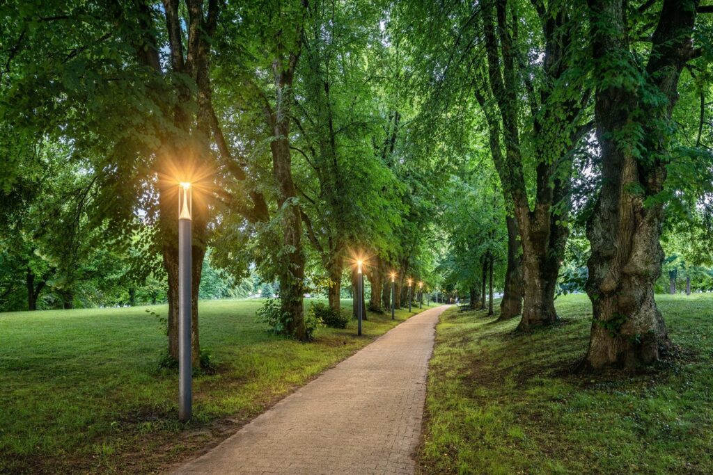 Parkstig upplyst av en rad eleganta, energieffektiva gatlyktor med stjärnformat varmt sken och robusta metallstolpar som skapar trygghet och atmosfär, perfekt för parker och stadsmiljöer, säljs av PROLJUS AB