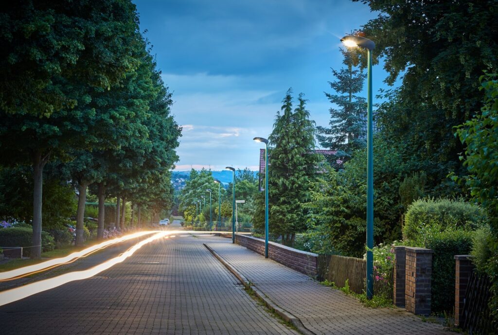 Kvällsbild av en allé med moderna PROLJUS AB-armaturer på gröna stolpar som sprider varm, jämn LED-belysning längs trottoaren och skapar trygg, energieffektiv och estetisk gatubelysning perfekt för bostadsområden