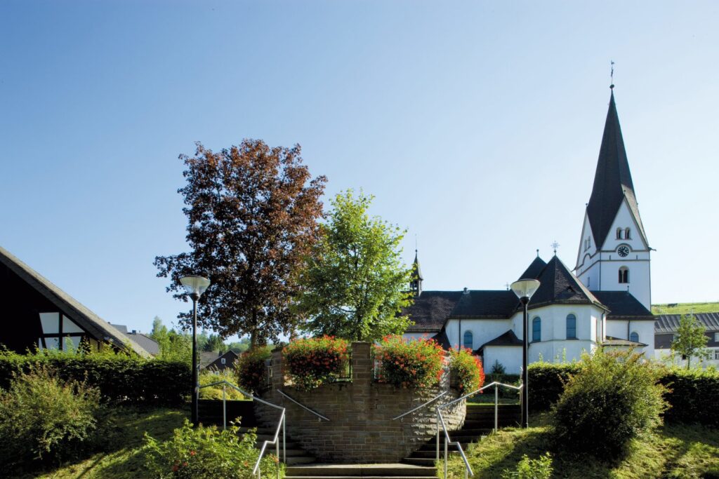 Två moderna gatlyktor från PROLJUS AB flankerar en stentrappa framför en vit kyrka, stilren energieffektiv LED-design som lyser upp entrén och visar produktens kvalitet och lämplighet för offentliga miljöer, kontakta PROLJUS AB för offert