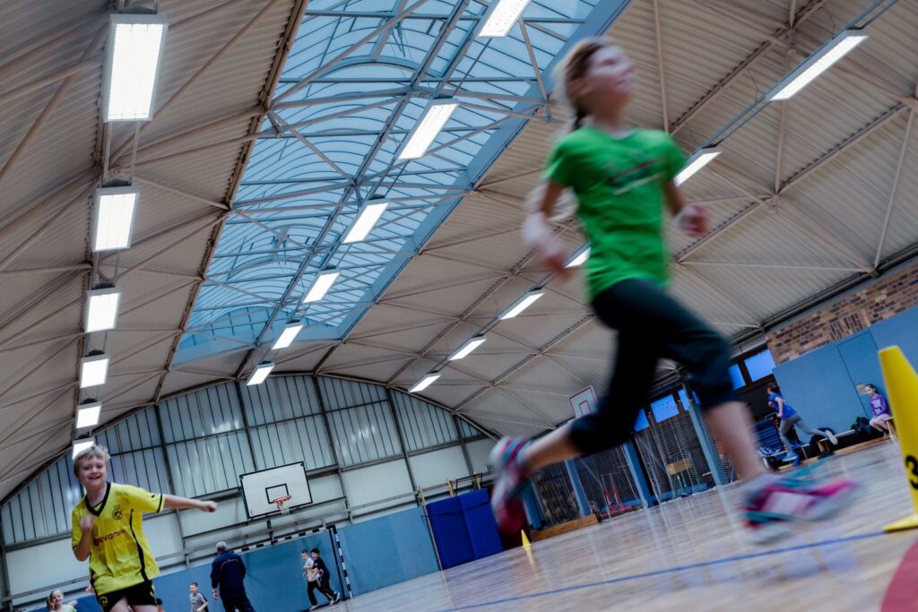Rader av rektangulära LED-armaturer i idrottshallens tak ger klart, jämnt och bländfritt ljus som lyfter aktiviteter och förbättrar säkerheten — energieffektiva och robusta belysningslösningar från PROLJUS AB