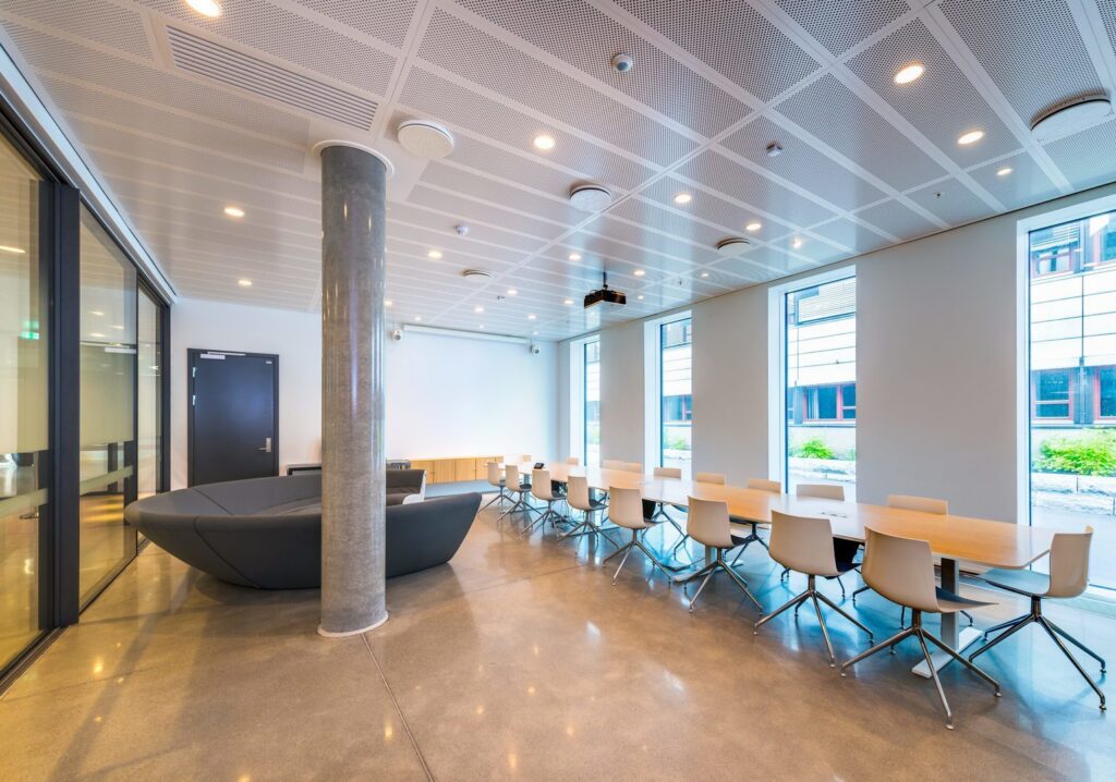 Konferensrum med diskreta infällda LED-downlights och cirkulära takarmaturer i perforerat undertak som ger jämnt varmvit arbetsljus över långt konferensbord och lounge, energieffektiva armaturer levererade och installerade av PROLJUS AB