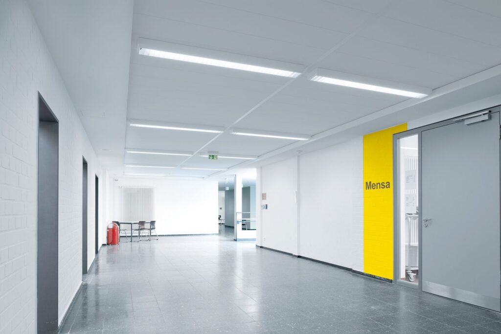 Korridor upplyst av infällda linjära LED-armaturer i taket som ger jämnt bländfritt vitt ljus och energieffektiv drift, en stilren lösning som lyfter skol‑ och kontorsmiljöer och som PROLJUS AB levererar med hög ljusstyrka, lång livslängd och skräddarsydda installationslösningar för moderna offentliga utrymmen