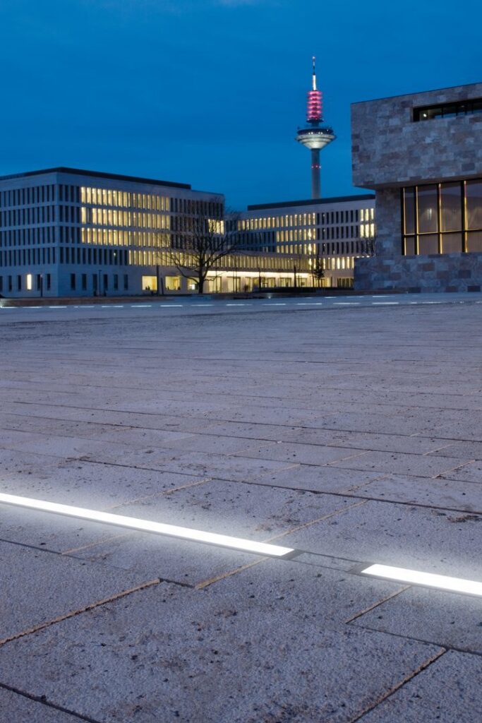 Kvällsbild av ett öppet torg med slanka inbyggda LED-linjer från PROLJUS AB som markerar gångstråk och skapar en modern, energieffektiv och robust belysningslösning idealisk för offentliga miljöer och kommersiella anläggningar