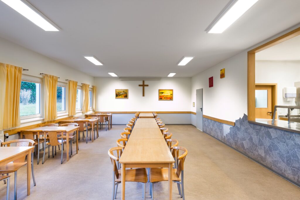 Rektangulära, energieffektiva LED-armaturer i taket som ger jämn, bländfri belysning i en matsal och demonstrerar PROLJUS ABs moderna belysningslösningar för skolor, församlingar och offentliga miljöer