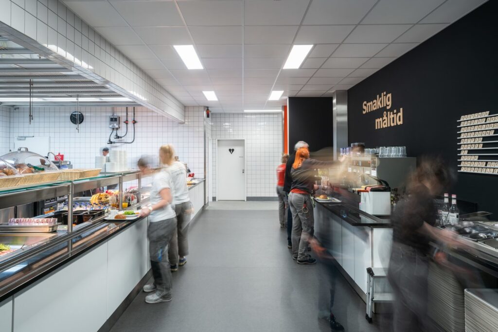 Cafeteriakök belyst av jämnt fördelade rektangulära inbyggda LED-paneler i undertaket som ger klart, bländfritt och energieffektivt arbetsljus från PROLJUS AB — moderna armaturer som ökar säkerheten, förbättrar produktiviteten och minskar energikostnader