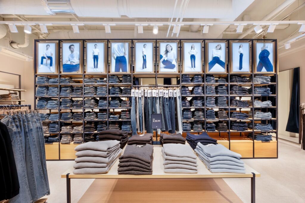 Butiksinteriör med välsorterade jeanshyllor och bordsdisplay upplyst av moderna spår- och infällda armaturer som ger jämnt riktat LED-ljus och lyfter fram texturer och färger, visar hur PROLJUS ABs energieffektiva och justerbara belysningslösningar skapar inbjudande atmosfär, förbättrar produktpresentation och ökar köpviljan