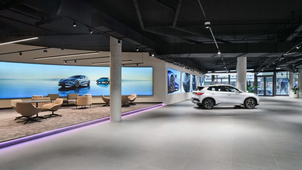 Stilren bilhall belyst av linjära hängande LED-armaturer, spårmonterade spotlights och färgskiftande LED-list i kanten som skapar dramatiskt fokus på fordon och loungeytor, en effektiv och försäljningsdrivande lösning från PROLJUS AB