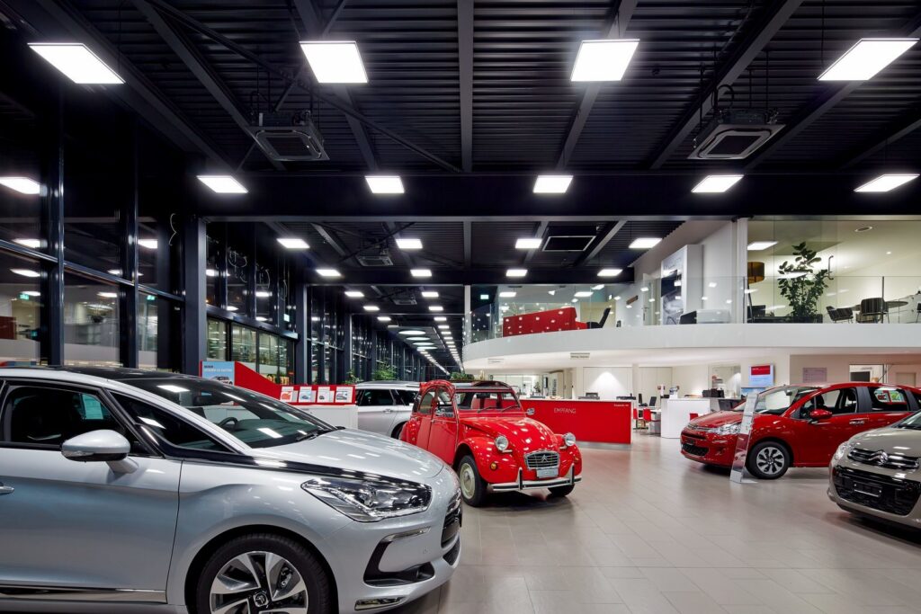 Energieffektiva LED-paneler i taket över ett bilshowroom som ger stark, jämn belysning för att framhäva lack och detaljer och visa PROLJUS ABs professionella belysningslösningar för försäljningsmiljö