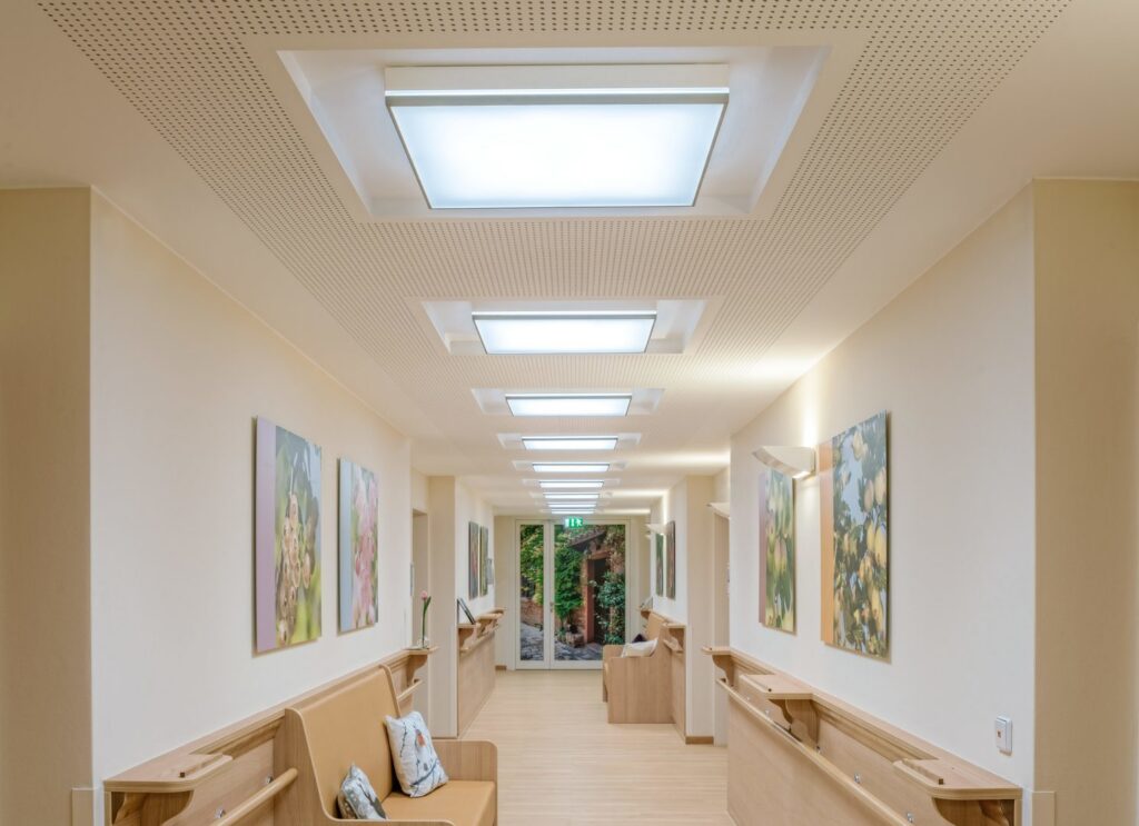 Rad infällda kvadratiska LED-armaturer i taket som ger jämnt, bländfritt och energieffektivt ljus i en korridor, idealiska för vård- och offentliga miljöer erbjuds av PROLJUS AB