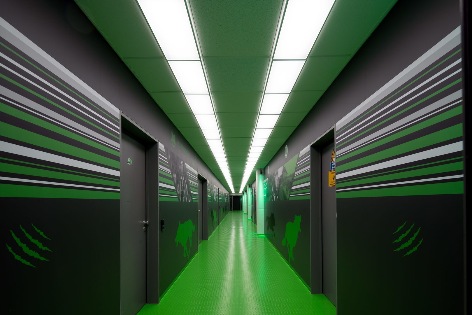 Lång korridor belyst av linjära, energieffektiva takpaneler från PROLJUS AB som ger jämnt, klart vitt ljus och framhäver lokalens gröna accenter och moderna industridesign