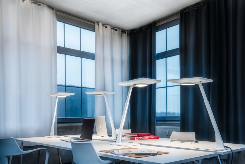 Fyra eleganta vita LED-skrivbordslampor från PROLJUS AB på ett modernt kontorsbord, justerbara armar och breda skärmar som ger jämnt arbetsljus, energieffektiva och stilrena lösningar som lyfter arbetsmiljön