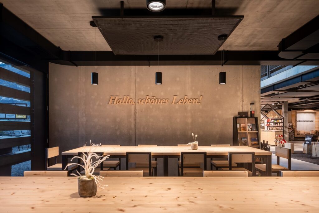 Varm LED-belysning från PROLJUS AB i modern lokal med tre svarta cylinderpendlar och en infälld spotlight som riktar ljus över långa träbord, stilren och energieffektiv lösning för restaurang, café och butiksmiljö