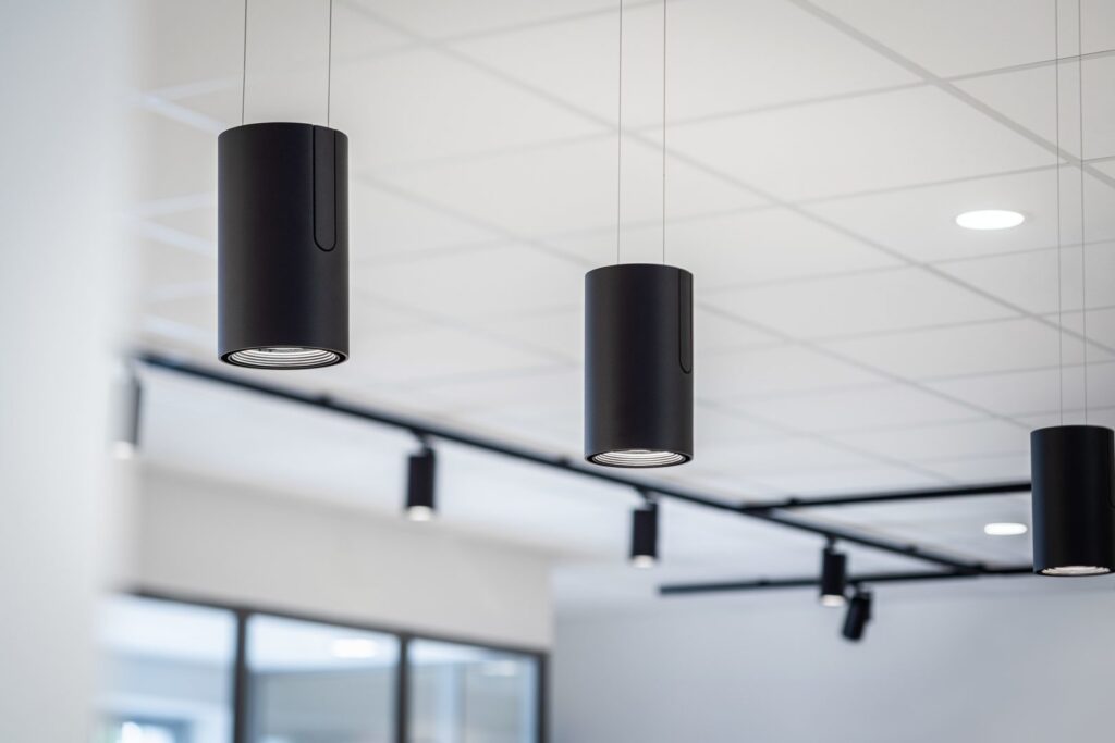 Svarta cylinderformade pendelarmaturer och spårmonterade spotlights i modern kontorsmiljö, energieffektiva och stilrena belysningslösningar perfekt för kontor och butiker från PROLJUS AB