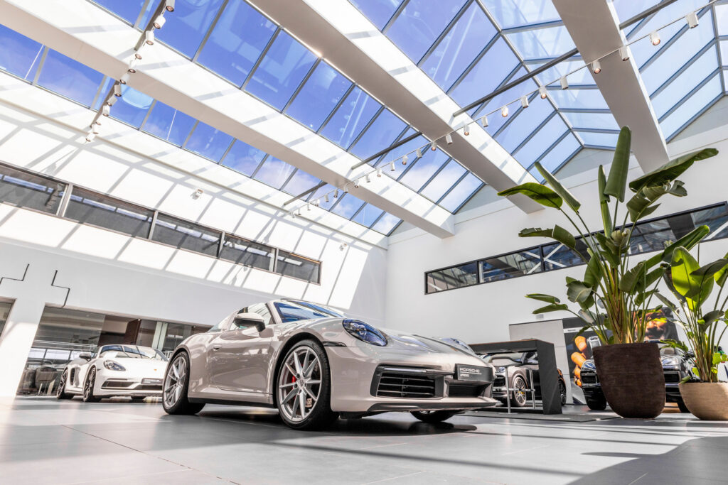 Modernt bilshowroom med generösa glastak och rad av justerbara skenspottar och spotarmaturer monterade på skenor som skapar fokuserat ljus över sportbilar, en elegant belysningslösning från PROLJUS AB som lyfter presentationen och ökar försäljningen