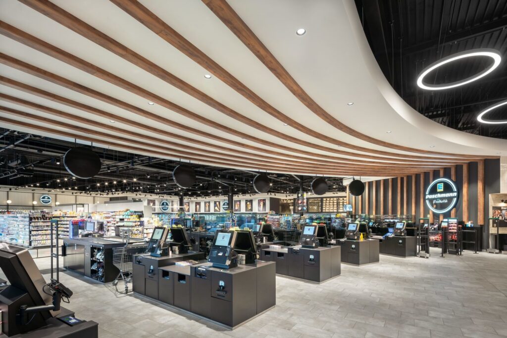 Modern butikskassa under ett träribbat tak med infällda spotlights och stora cirkulära LED‑ringar som ger jämnt, energieffektivt och stämningsfullt ljus perfekt för butiksmiljöer från PROLJUS AB