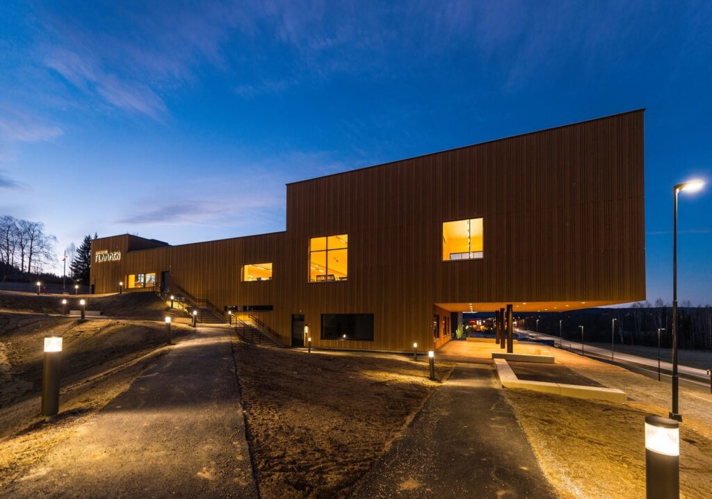 Kvällsbild av modern byggnad med upplyst gångväg och fasad av varma, energieffektiva pollarlampor och stolpbelysning som skapar trygghet och framhäver arkitekturen — välj PROLJUS AB