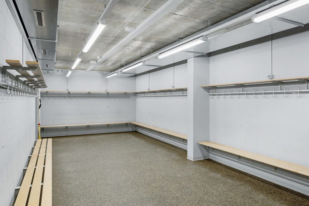 Linjära LED-armaturer från PROLJUS AB monterade i betongtaket i ett omklädningsrum, moderna energieffektiva och bländfria armaturer som ger jämn, kraftfull arbetsbelysning, robust minimalistisk design och enkel installation perfekt för sportanläggningar och industrilokaler