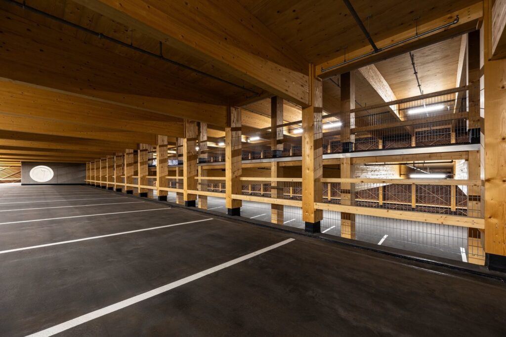 Träklädd parkeringsvåning upplyst av jämnt fördelade linjära LED-armaturer monterade i tak och på balkar, varmt klart ljus som framhäver konstruktionen och demonstrerar PROLJUS AB:s energieffektiva kommersiella belysningslösningar perfekt för säkra och estetiska miljöer