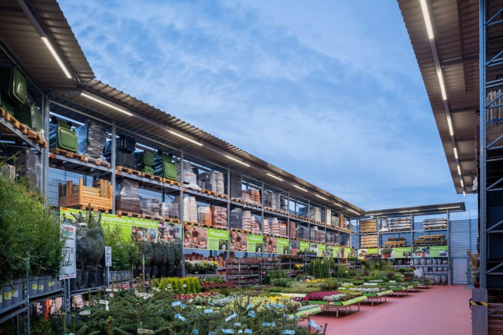 Ljust upplyst trädgårdsmästeri med långa väderbeständiga LED-armaturer monterade under tak som ger jämn energieffektiv belysning över plantbord och hyllor, idealiskt för butiksmiljöer och saluförs av PROLJUS AB som professionella lösningar för att framhäva produkter och sänka driftkostnader