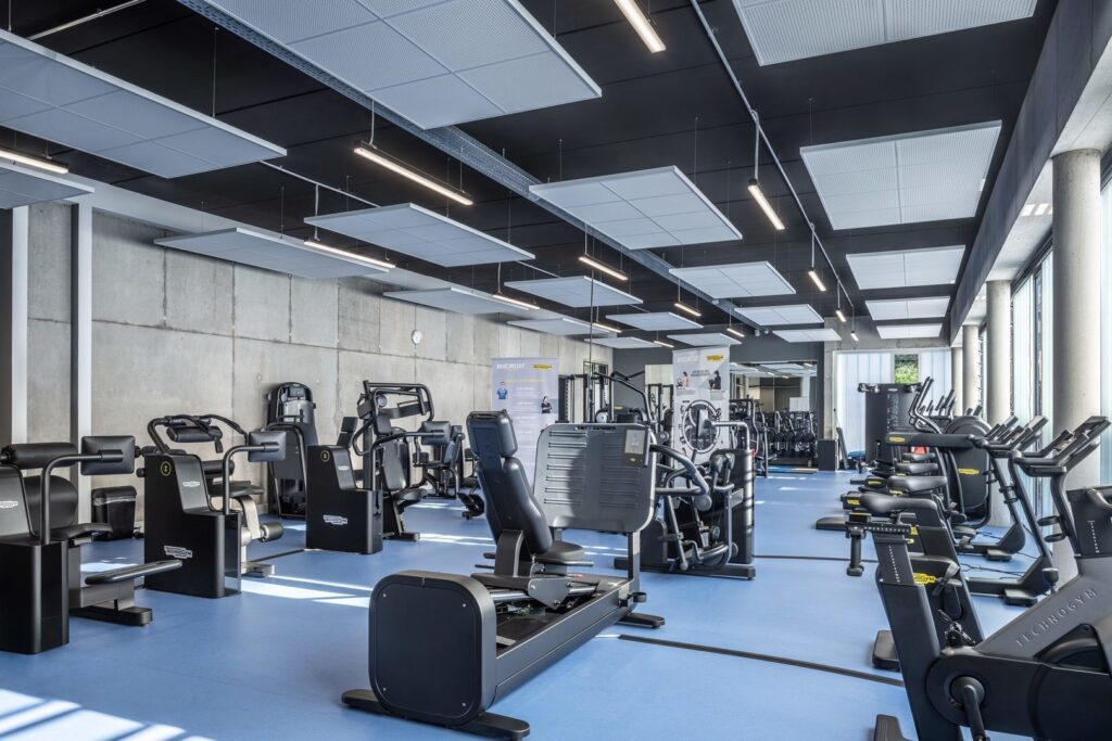 Modern gyminteriör upplyst av långa linjära pendellampor och svävande rektangulära LED-armaturer från PROLJUS AB som levererar jämnt, dagsliknande och energieffektivt ljus för förbättrad träning och stilren, professionell atmosfär
