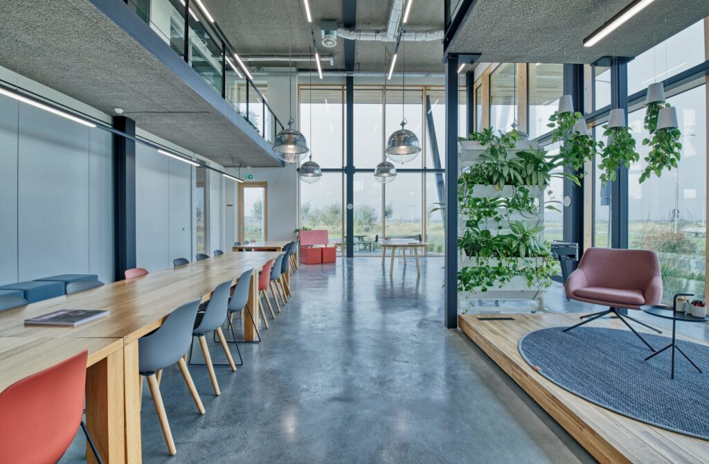 Öppen kontorsmiljö belyst av PROLJUS AB:s moderna armaturer: stora kromade pendellampor i kupform över mötesbordet tillsammans med långa linjära LED-takarmaturer som ger jämnt, bländfritt och energieffektivt arbetsljus och förhöjer den skandinaviska inredningen, ett stilrent belysningsval för företag