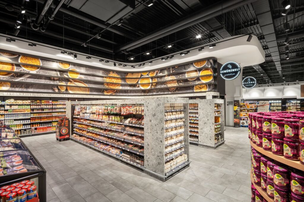 Modern mataffärsinteriör med svart öppet tak och diskreta spår- och infällda armaturer som sprider varm, jämn ljusbild för att framhäva hyllor och produkter och förbättra kundupplevelsen, belysning från PROLJUS AB