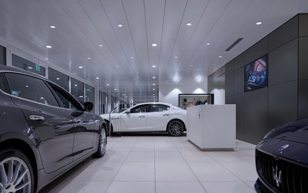 Bilshowroom med rader av jämnt fördelade infällda takspotlights som ger klart vitt, skuggfritt ljus och speglingar i bilarnas lack en lyxig atmosfär där PROLJUS AB:s armaturer framhäver detaljer och ökar försäljningsintrycket i lokalen