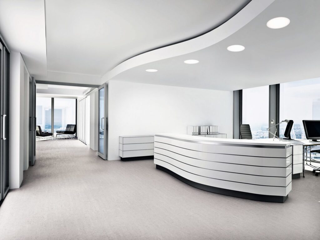 Eleganta runda infällda LED-armaturer i taket över modern kontorsmottagning ger jämnt, energieffektivt ljus och lyfter den minimalistiska inredningen från PROLJUS AB