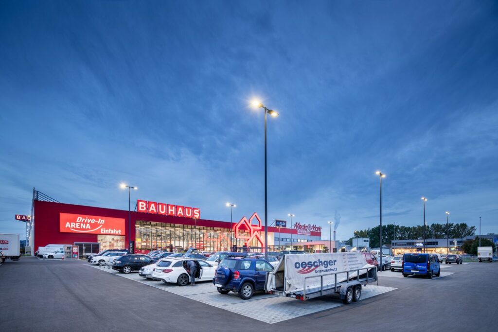 Höga moderna LED-stolpar lyser upp en butiksparkering i skymning med klart, jämnt och energieffektivt ljus, PROLJUS AB levererar dessa robusta utomhusarmaturer som ökar säkerhet och kundattraktion