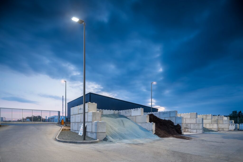 Tre höga, energieffektiva PROLJUS-armaturer på stolpar lyser upp en industriell lagergård med klart och jämnt LED-ljus och visar modern, robust design och tillförlitlighet idealisk utomhusbelysning från PROLJUS AB