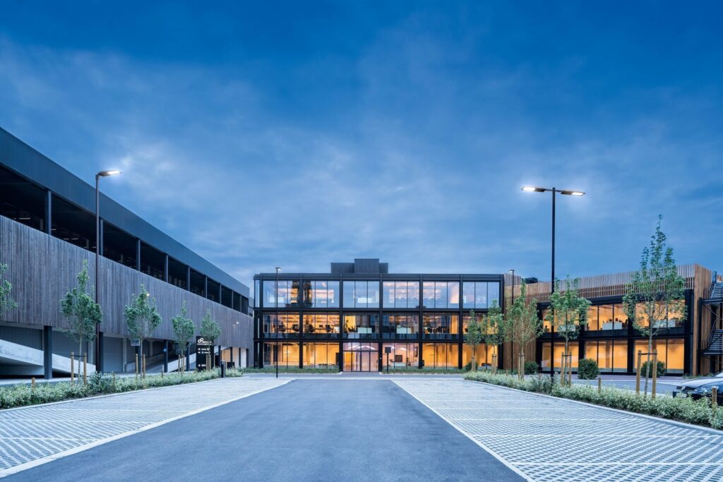 PROLJUS AB:s moderna LED-armaturer lyser upp parkeringsytan och entrén till en glasad kontorsbyggnad i blå skymning, riktade energieffektiva belysningslösningar som framhäver arkitekturen och skapar trygghet och ett professionellt intryck