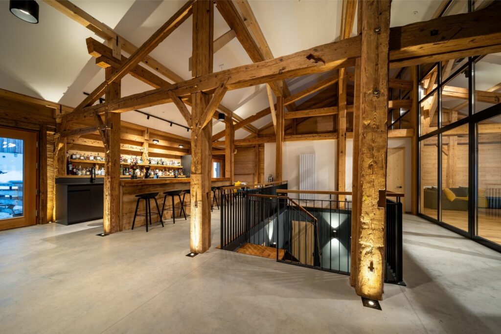 Belysningslösningar från PROLJUS AB: varma golvinfällda uplights som accentuerar rustika träbjälkar, spår- och hyllarmaturer vid baren samt vägg‑ och trappinfällda spotlights som skapar atmosfär och visar produktdesign och energieffektivitet