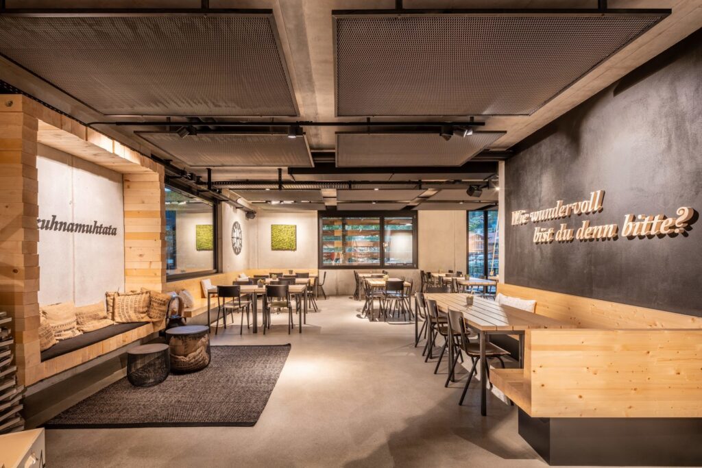 Modern restauranginteriör med svarta takmonterade skensystem och riktbara spotlights från PROLJUS AB som ger varmt, jämnt ljus över bord och framhäver trädetaljer, kompletterat av akustiska takpaneler för optimal ljudmiljö, kontakta PROLJUS AB för skräddarsydda och energieffektiva belysningslösningar