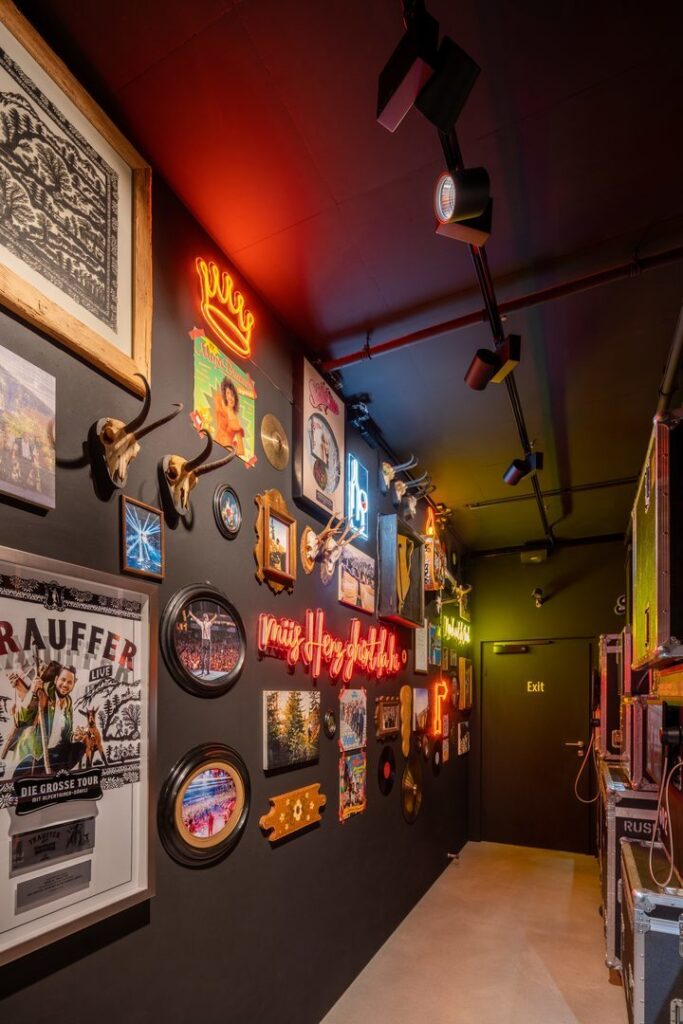 Korridor med mörka väggar upplyst av PROLJUS ABs riktbara takskenor och spots samt färgstarka neonljus som skapar varm, stämningsfull accentbelysning och framhäver väggdekoren, kontakta PROLJUS AB för anpassade belysningslösningar