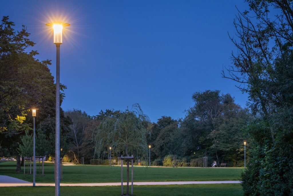 Kvällsbild av en park upplyst av eleganta och energieffektiva parkarmaturer från PROLJUS AB med varmt jämnt sken som framhäver robust design och trygg belysning för stads- och parkmiljöer