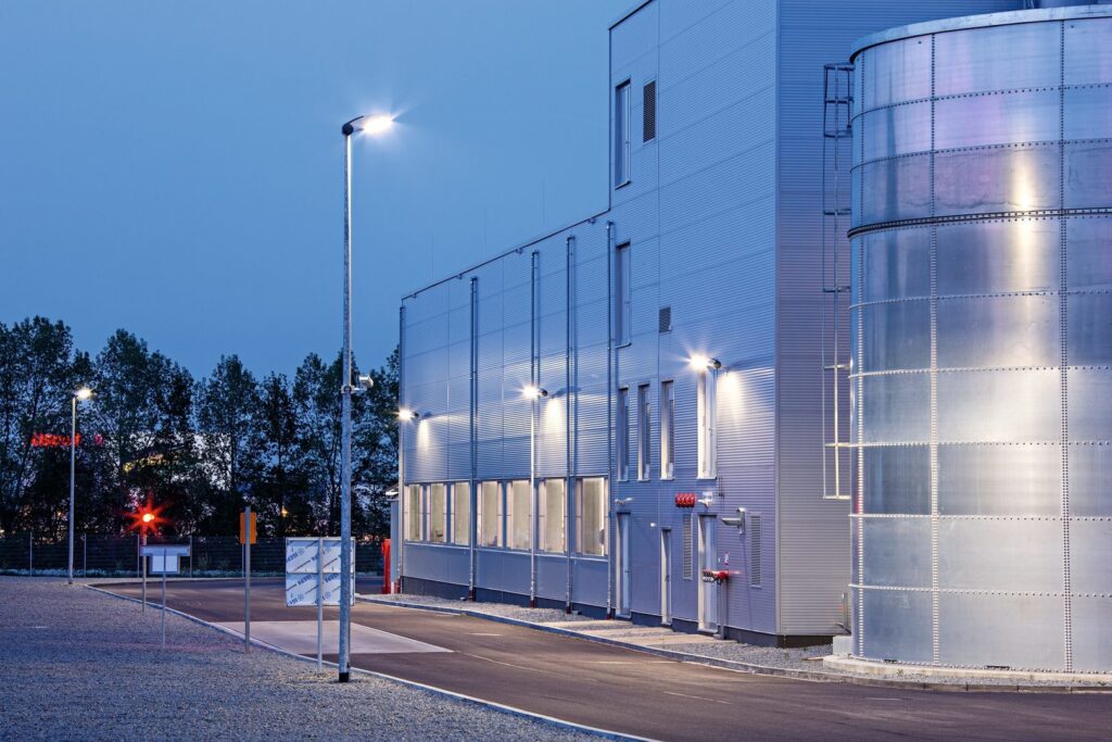 Skymningsbild av industrifasad upplyst av PROLJUS ABs moderna LED-stolpar och väggarmaturer som ger klart, kallvitt ljus och jämn fasadbelysning, energieffektiva och robusta lösningar för industriella miljöer