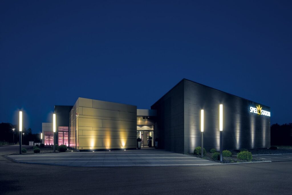 Nattbild av modern byggnad belyst av PROLJUS ABs slanka vertikala pollare och infällda fasadspotlights som ger ett jämnt varmvitt LED-sken, framhäver arkitekturens linjer och erbjuder energieffektiv, kommersiellt attraktiv ljussättning