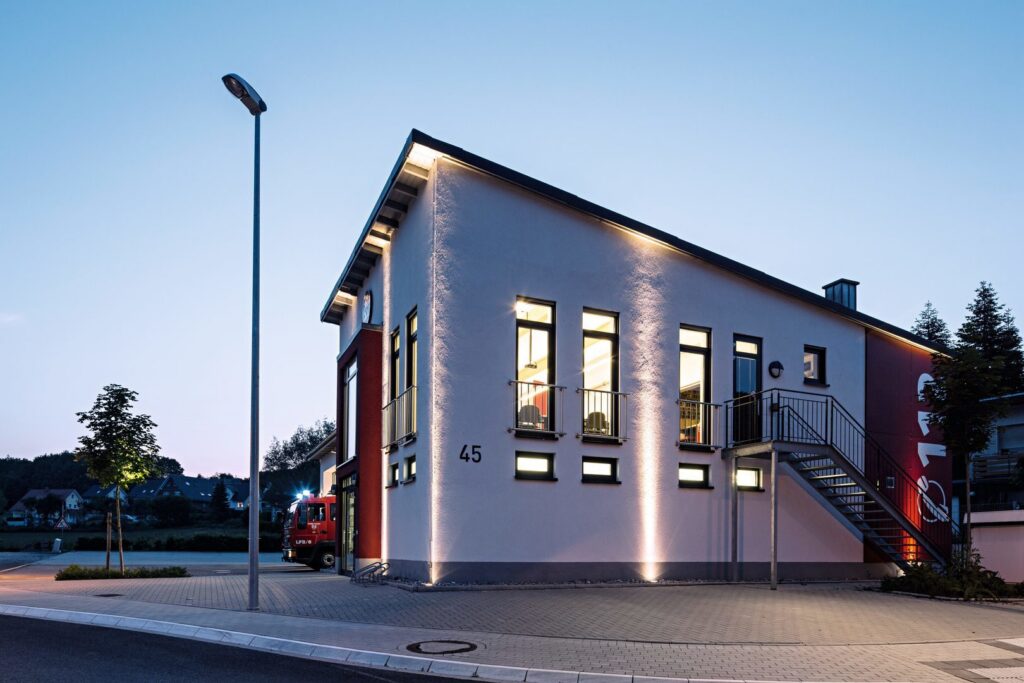 Kvällsbild av modern byggnad upplyst av PROLJUS ABs LED-armaturer med diskreta mark- och väggstrålkastare som tvättar fasaden i varm, jämn lyster, integrerade fönster- och trappbelysningar samt linjär tak-LED som framhäver arkitekturen, energieffektiv och säljande lösning för kommersiella fastigheter