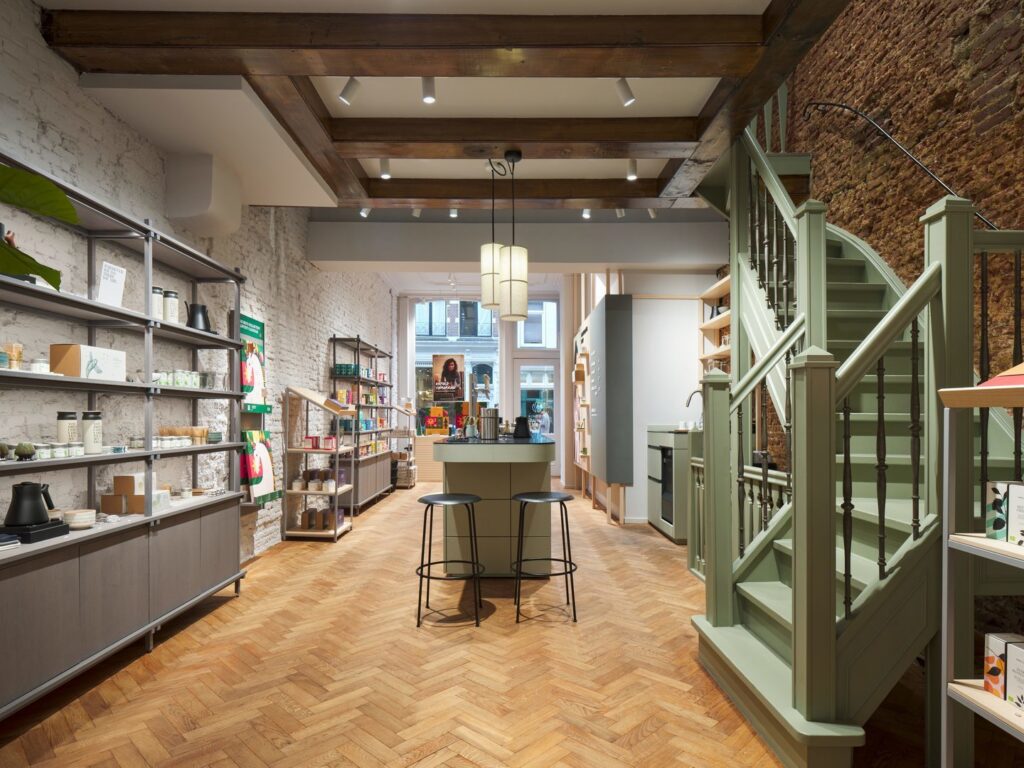 Modern butikslokal med synliga träbjälkar där cylindriska pendellampor över en central disk och flera takmonterade spotlights i bjälkarna ger varmt, riktat ljus för optimal varuexponering, perfekt exempel på PROLJUS ABs butikbelysning, kontakta PROLJUS AB för skräddarsydda belysningslösningar