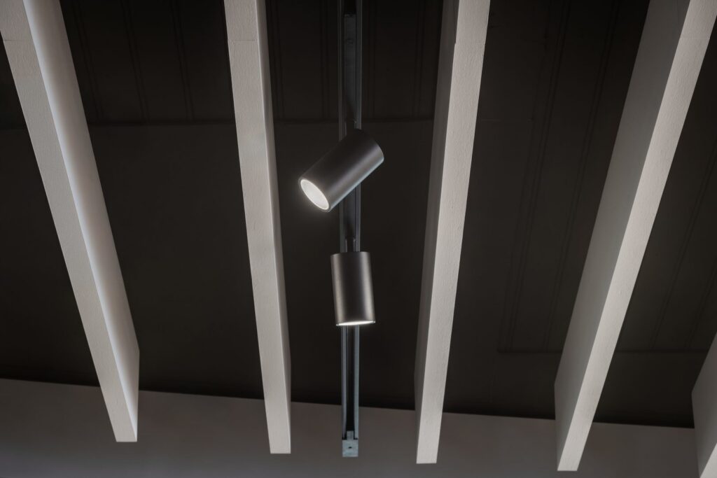 Elegant spårmonterad armatur med två cylindriska svarta LED-spotlights installerade mellan vita takbjälkar, riktbar och energieffektiv belysning idealisk för butik och kontor från PROLJUS AB