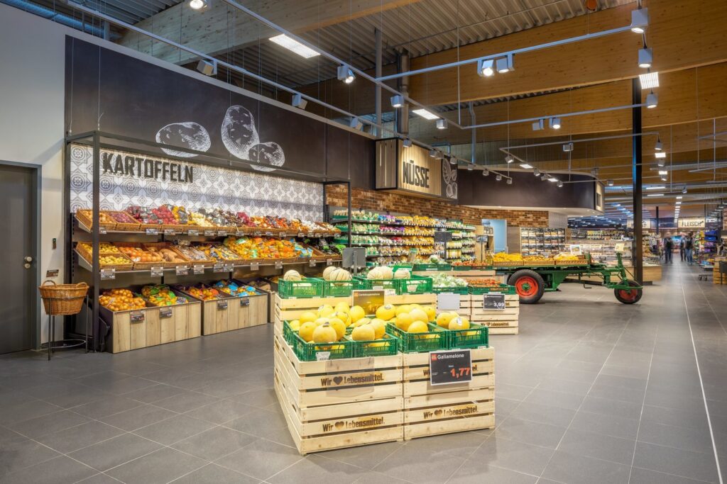 Stort, väl upplyst supermarket med frukt- och grönsaksavdelning belyst av moderna takskenor och riktade spotlights som ger jämn, varm färgåtergivning och framhäver varorna, energieffektiva lösningar från PROLJUS AB som ökar försäljningen i butik