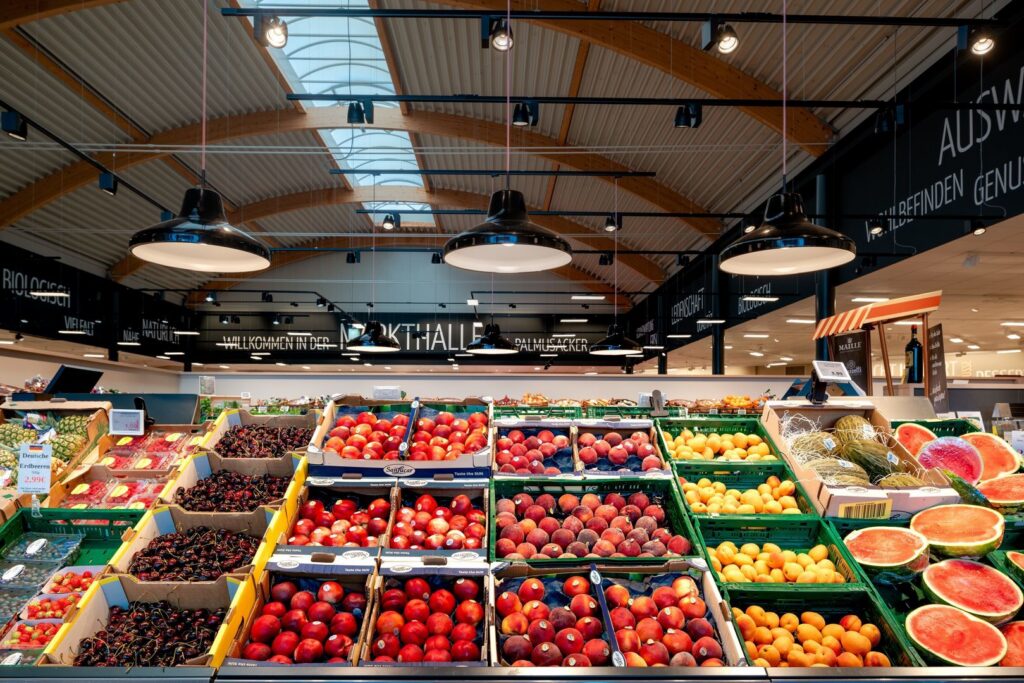 Fyra stora svarta industrilampor hänger i rader över en fruktdisk och sprider varmt, jämnt ljus som framhäver färgerna, en idealisk butikslösning från PROLJUS AB