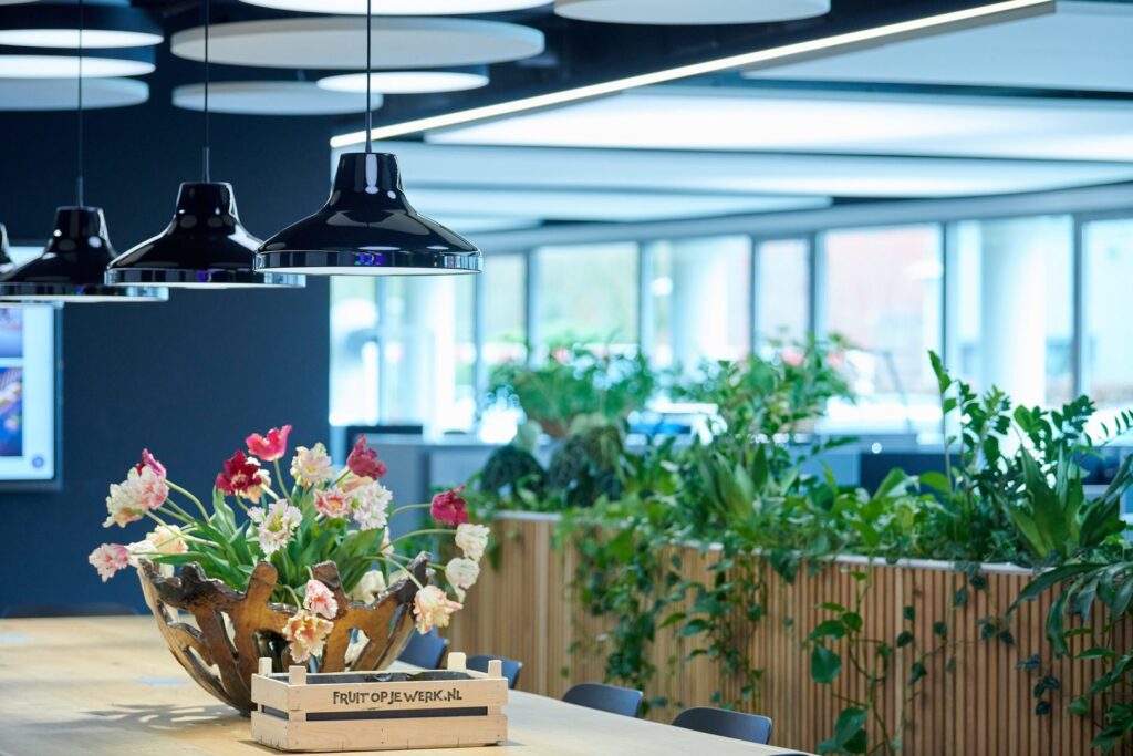 Svarta moderna hänglampor i fokus från PROLJUS AB, blanka energieffektiva LEDarmaturer som ger jämn kontorsbelysning över ett ljust coworkingbord med växter och blommor