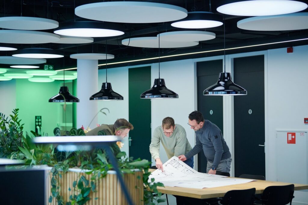 Svarta takpendlar från PROLJUS AB lyser över ett mötesbord i ett modernt kontor och kombinerar elegant design och energieffektiv belysning med cirkulära takpaneler, en säljfrämjande lösning för företag som vill förhöja arbetsmiljön