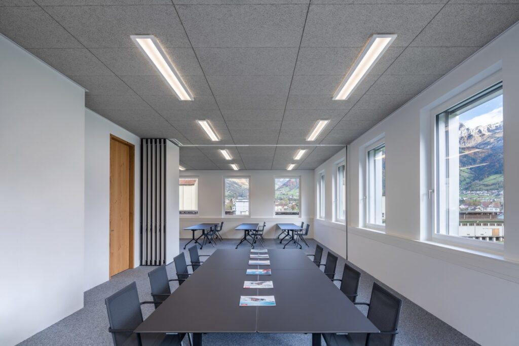 Moderna infällda linjära LED-armaturer i undertaket som ger jämn, bländfri belysning över konferensbordet i ett ljust kontorsrum, energieffektiva och stilrena lösningar från PROLJUS AB som förbättrar arbetsmiljön och minskar driftkostnaderna