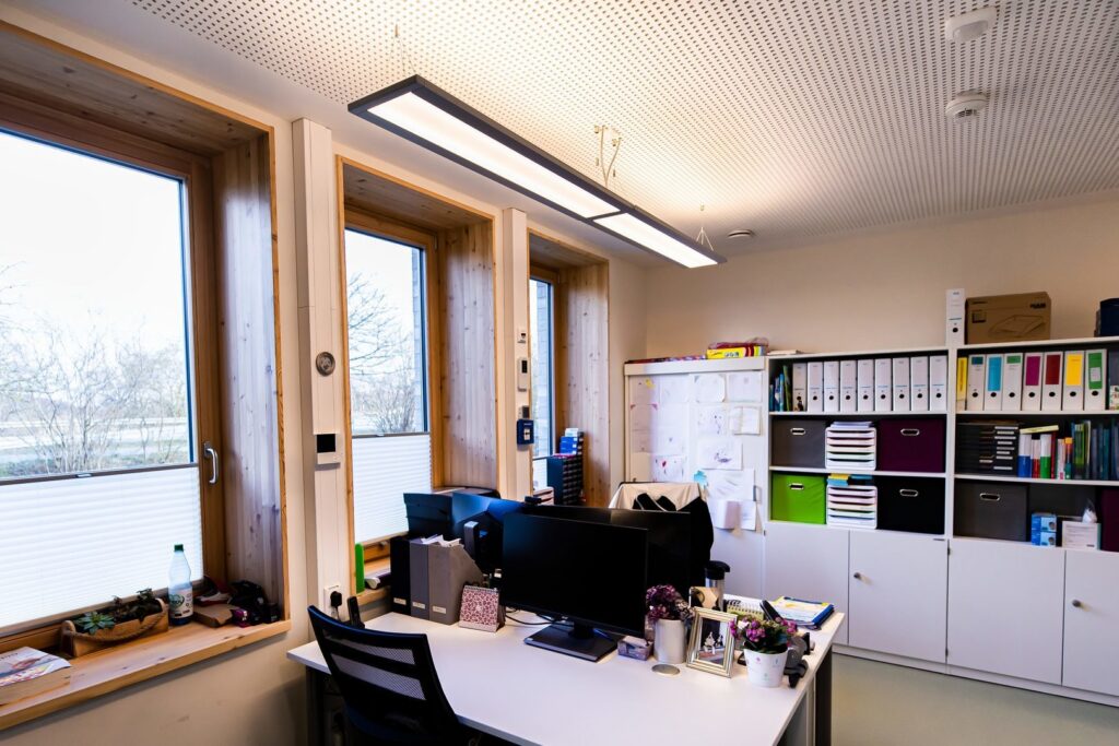 Två slimmade rektangulära takarmaturer från PROLJUS AB hänger i taket och sprider jämnt, energieffektivt och bländfritt varmt vitt ljus över ett modernt kontor, en elegant och kostnadseffektiv belysningslösning för arbetsmiljöer